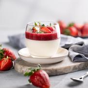 Panna cotta with strawberry and cream in glass with fresh berries on a marble board on a light background with shadow.
